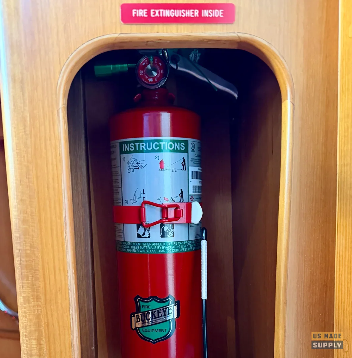 Red Buckeye Halotron clean-agent fire extinguisher mounted upright in a varnished teak locker inside a boat cabin, with a red and white Fire Extinguisher Inside placard on the door above it