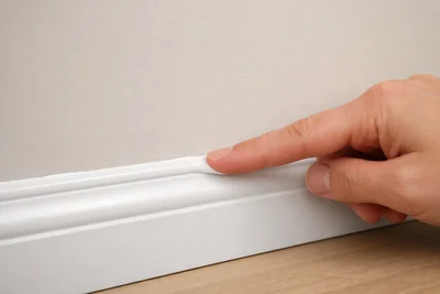 Finger smoothing white acrylic latex caulk along baseboard trim