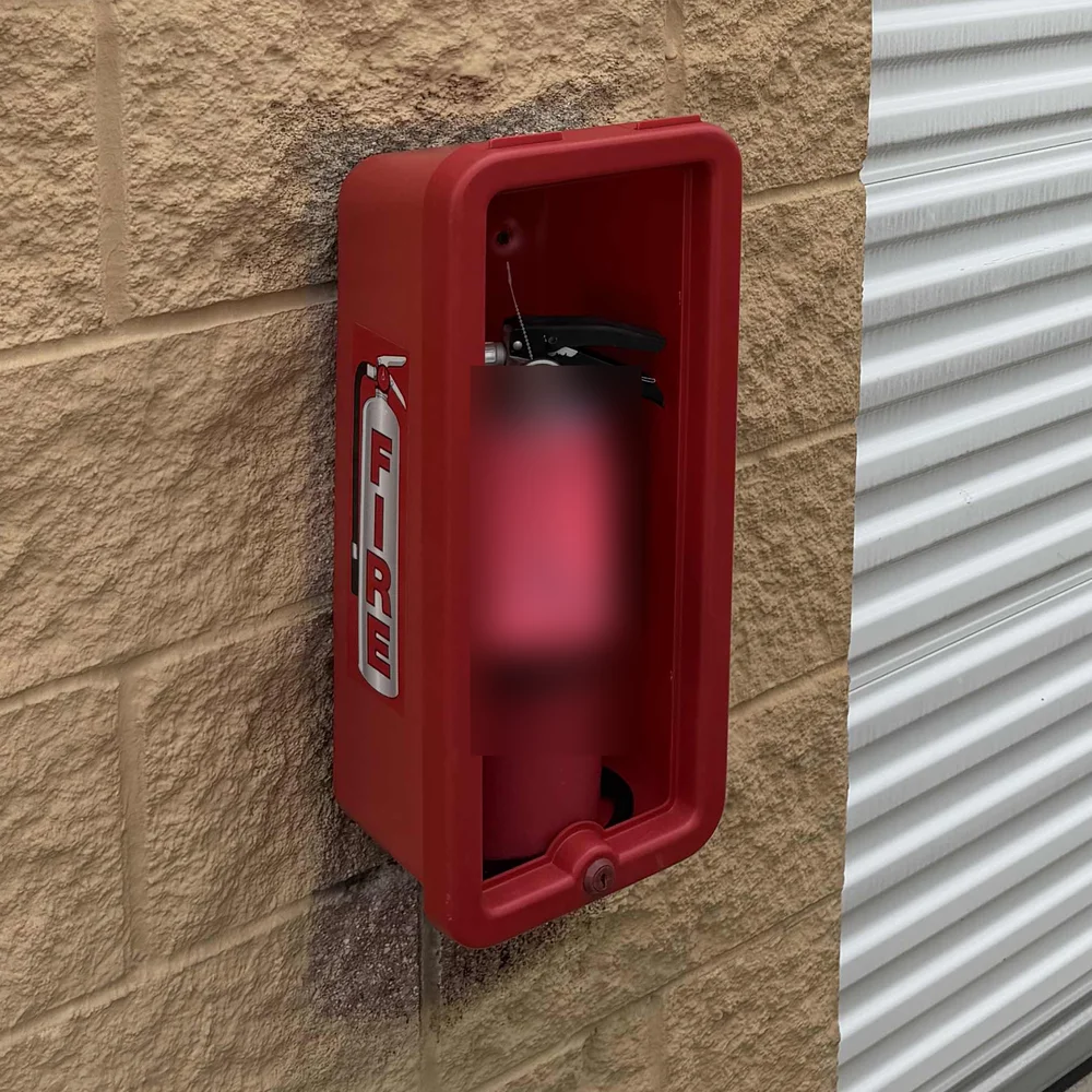 A red fire extinguisher cabinet labeled FIRE on a concrete-block wall beside a drive-up self-storage unit door