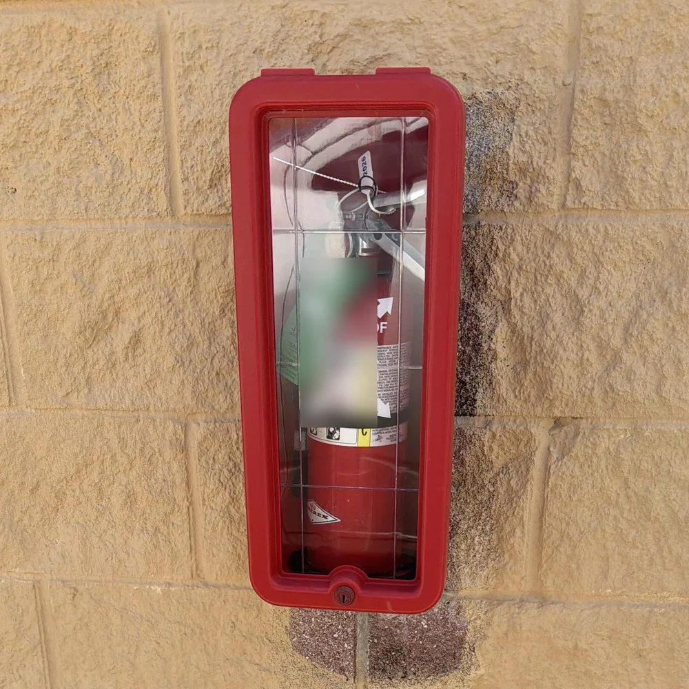 A red surface-mounted fire extinguisher cabinet on a concrete-block self-storage building wall